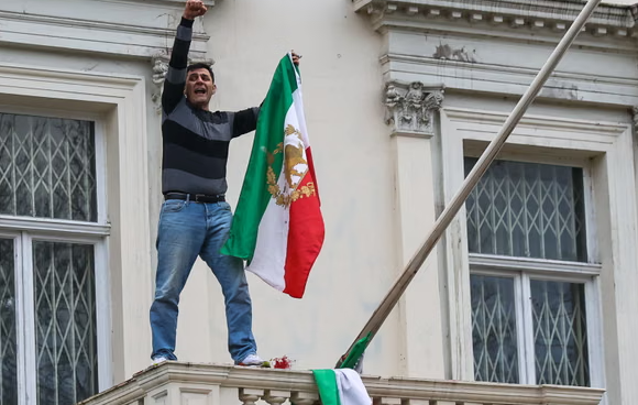 متظاهر يستبدل علم إيران براية “الأسد والشمس” في لندن (فيديو)